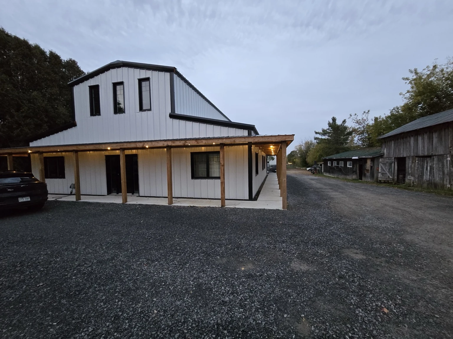 White barndominium with a raised centre peak, east and west wings and timber porch