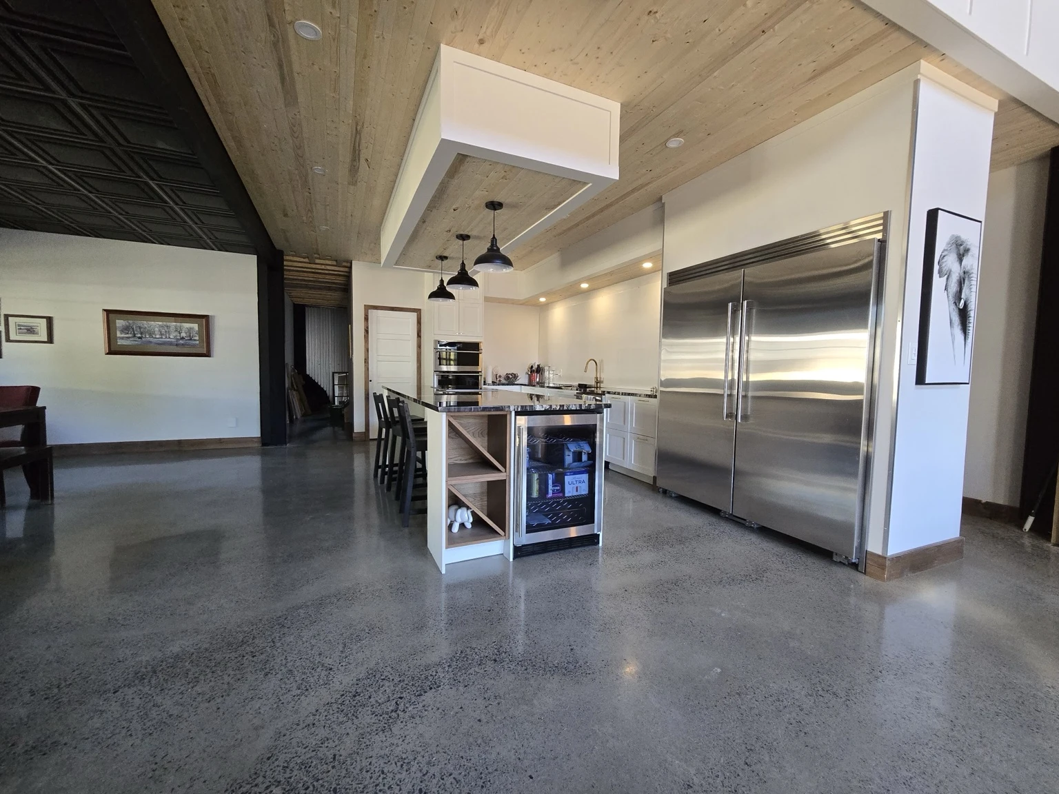 White kitchen with a large island, timber ceiling and stainless steel refrigerator